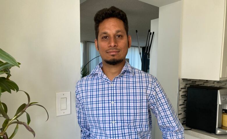 Raulson Sequeira, wearing a checkered shirt, stands in front of a doorway. 