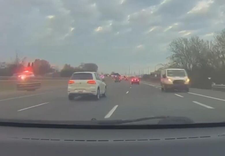 A white van on the shoulder of a highway. A police vehicle with lights flashing is on the other side of the median.