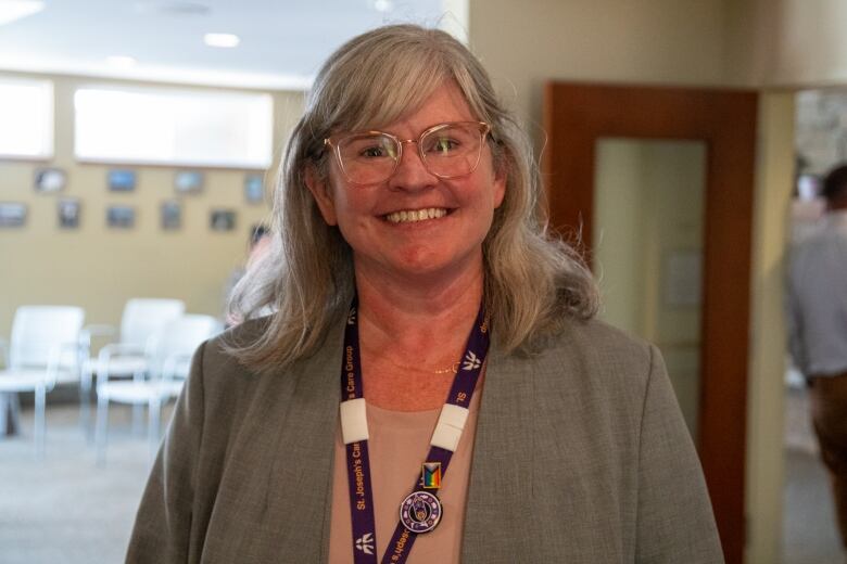 A close-up of a person wearing a purple lanyard is seen standing in a room, smiling.