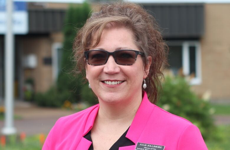 woman with sunglasses and pink blazer smiles at camera