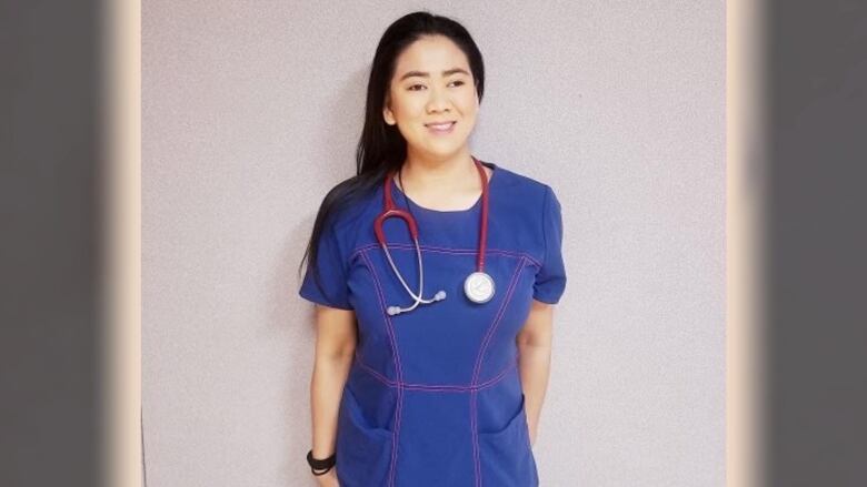 A woman nurse with long black hair is seen posing in blue scrubs with a red stethoscope over her neck.