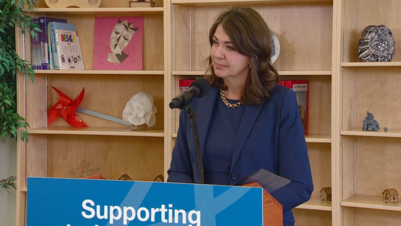 Premier Danielle Smith standing at a microphone at a press conference.