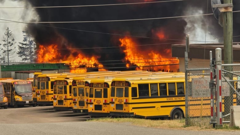 Smoke and fire rises behind a row of school buses.