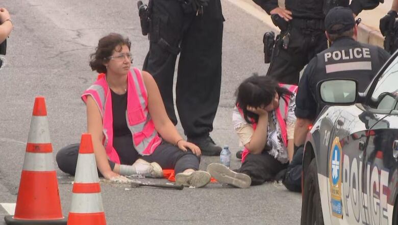 People sit on a road surrounded by police.