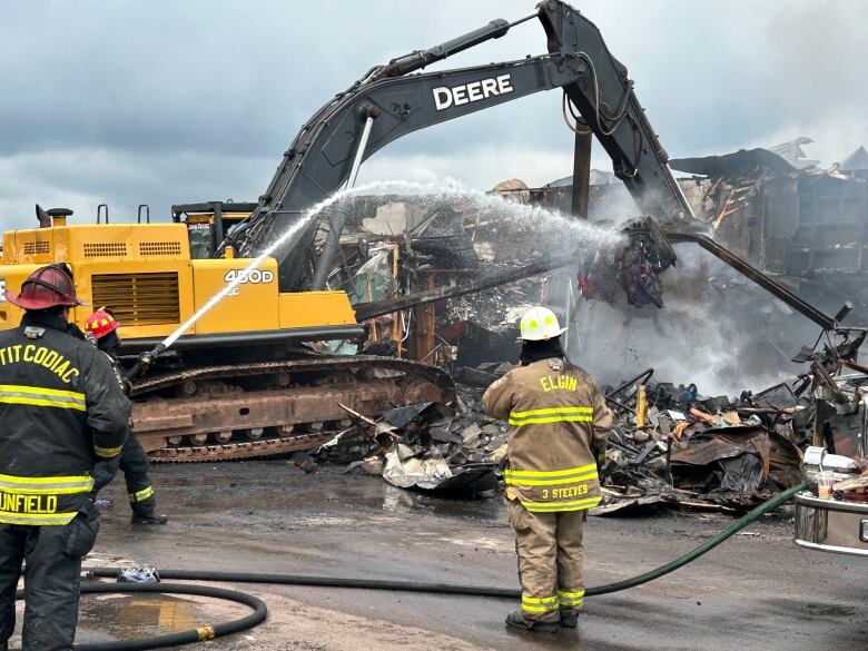 A fire scene. Water being thrown on a burnt building, can also see an excavator in action.