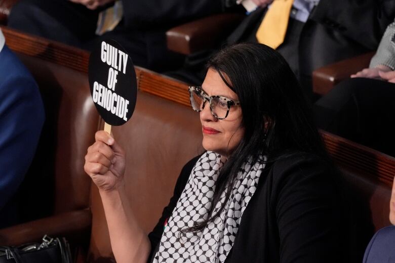 A person seated holds up a small sign that reads, 'Guilty of genocide.'