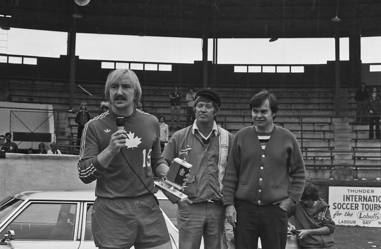 A man holding a trophy speaks into a microphone.