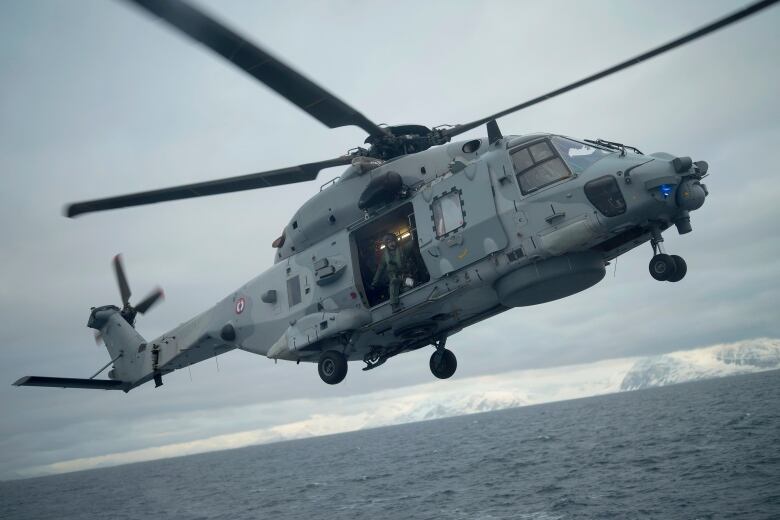 A French sailor is seen at the door of a helicopter as it takes off from the French navy frigate Normandie during a patrol in a Norwegian fjord, north of the Arctic circle, Thursday March 7, 2024.