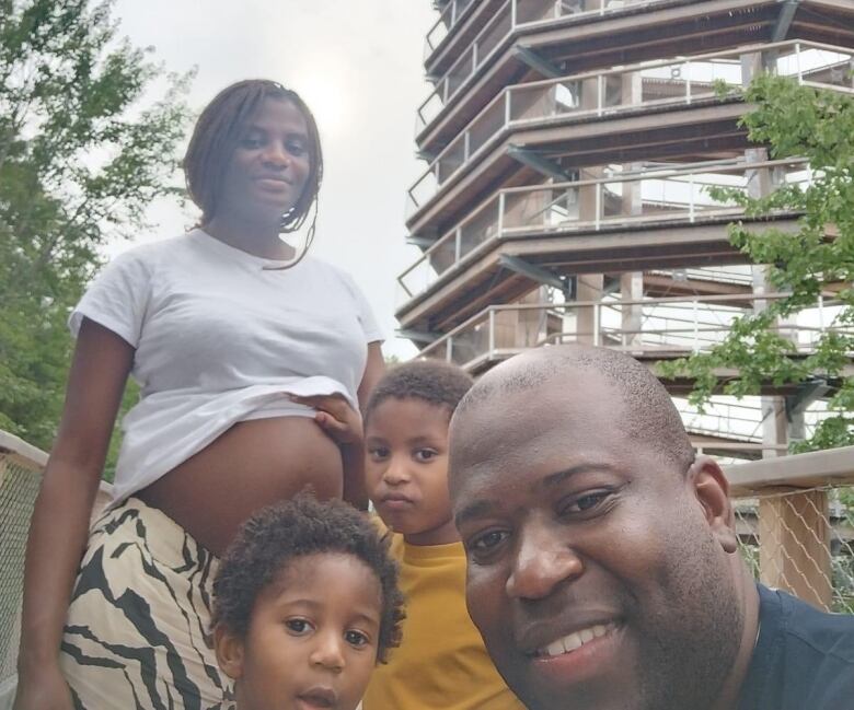 A pregnant woman poses with her husband and two young songs in front of a large structure. 