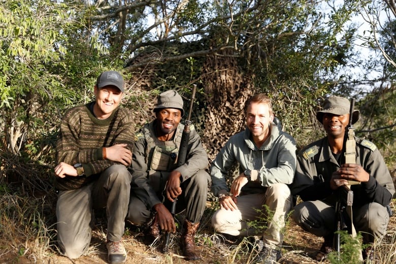 Four men kneel and crouch in front of some bushes