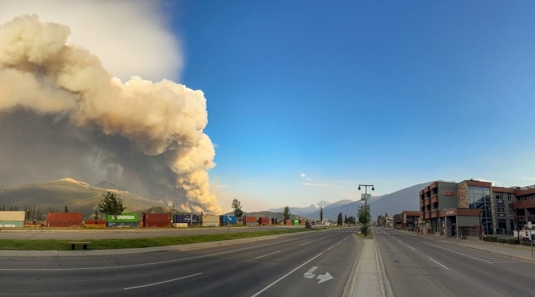 Smoke billows in the distance in this view of a street with mountains in the distance.