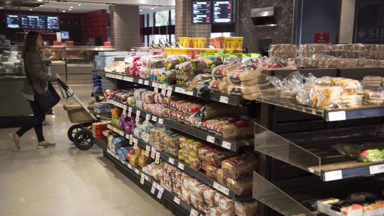 A female shopper is shown in a grocery store in an aisle next to what appear to be bread and bakery products.