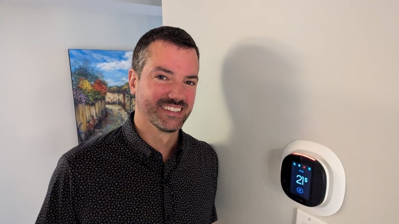 Man smiling next to thermostat on wall in hallway