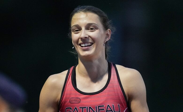 A woman in a track uniform smiles at a camera.