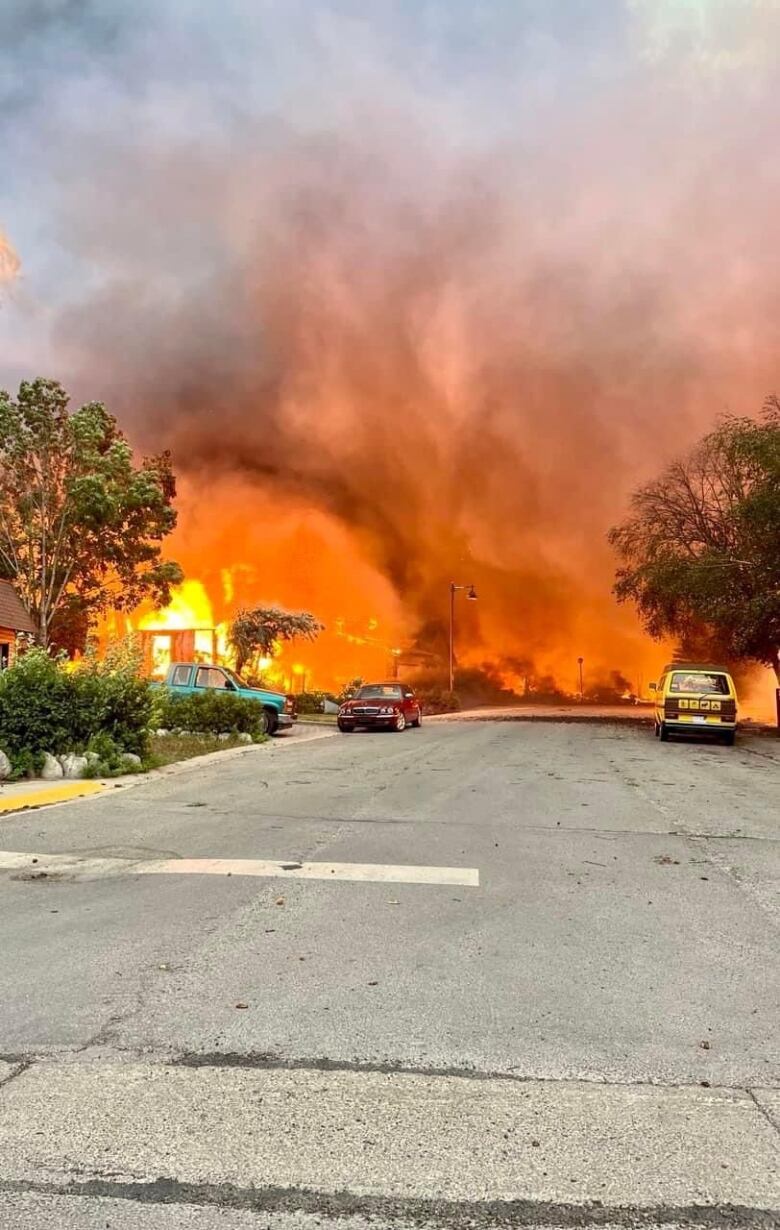 Flames whip across a street as a house burns.