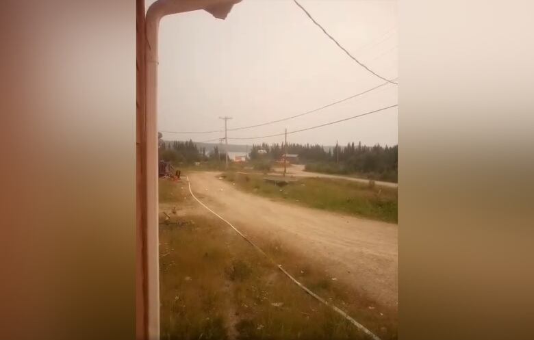 An unpaved road is in front of a porch, smoke covers the air and the sky is grey.