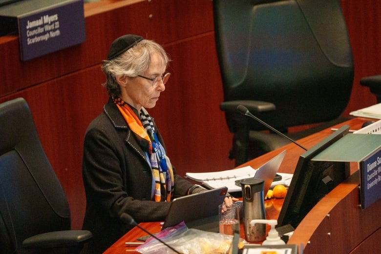 A woman in a black jacket sits in the Toronto city council chambers.