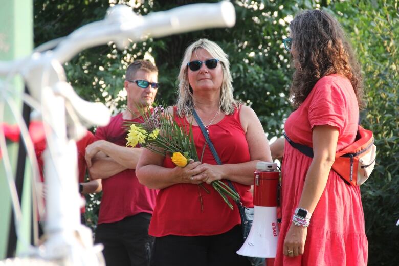 A woman in red cradles some flowers as she looks forward at a bike painted in white.