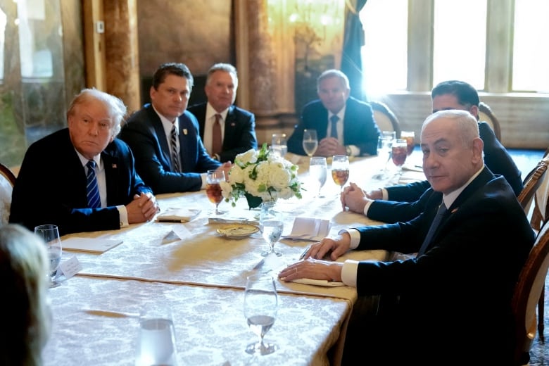 Men in suits sit around an ornate dining table.