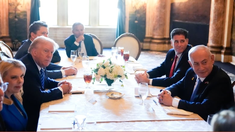 Men in suits sit around an ornate dining table.