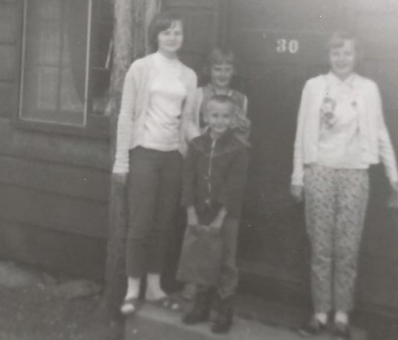 An old black and white photo show 4 siblings, one boy and three girls standing in front of the door of a cabin with the number 30 on it.