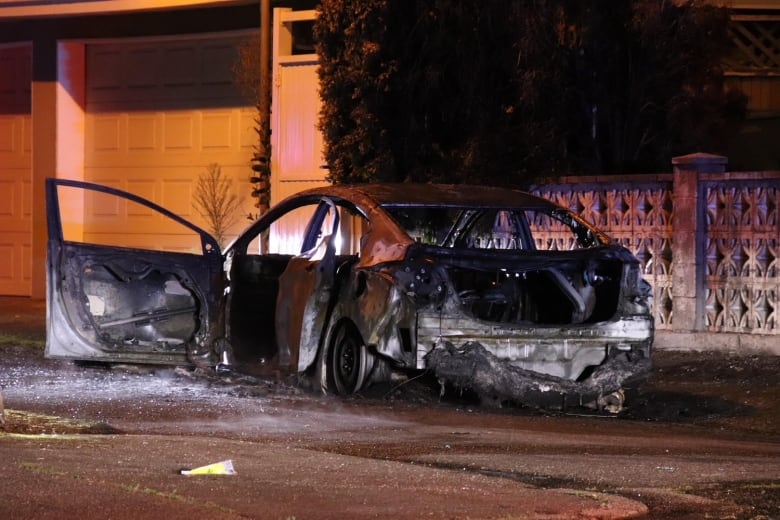 A burned-out sedan car is seen on a residential street.