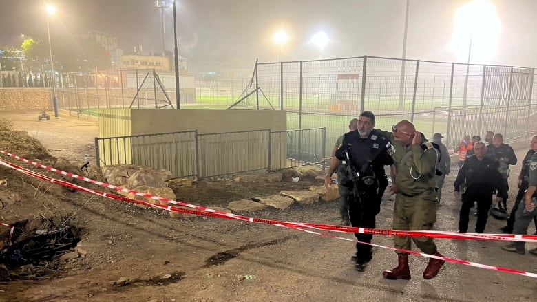 Law enforcement gather behind caution tape and near a soccer damaged soccer field.