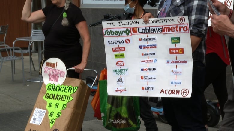 A group of people hold signs as they walk. A woman wearing a dark navy shirt holds a sign that reads 