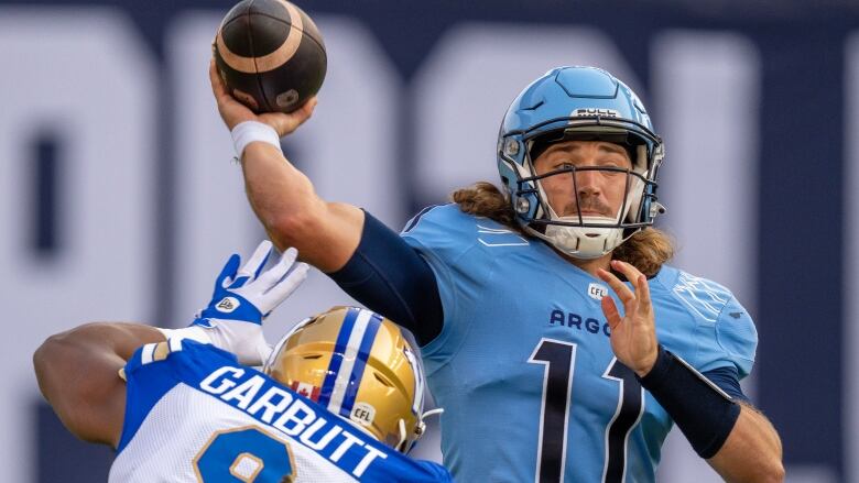 A football player is about to throw the ball as an opposing player tries to stop him.