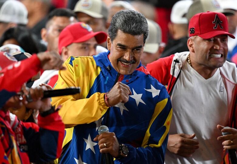 A man in a purple and yellow track suit smiles. He's flanked in crowd by other smiling men.