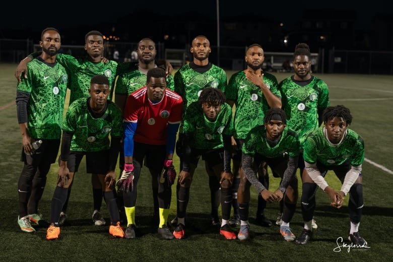 11 men wearing bright green jerseys pose in their soccer uniforms on the pitch at night