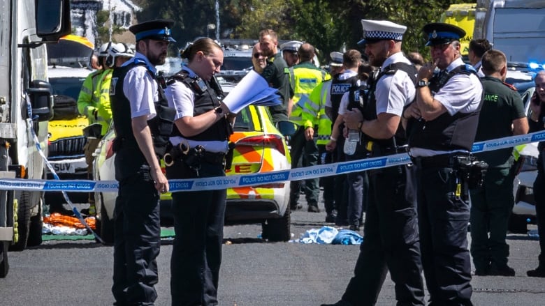 Police officers stand behind police tape on the street.