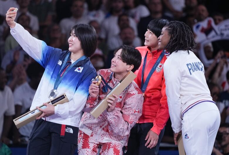 Four female athletes are seen taking a selfie with medals around their necks.