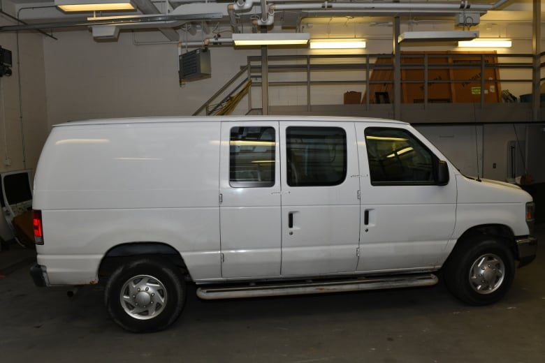 A white Ford van is seen from the side in a garage