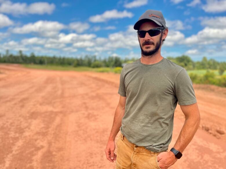 A man with sunglasses and a hat stands in a field. 