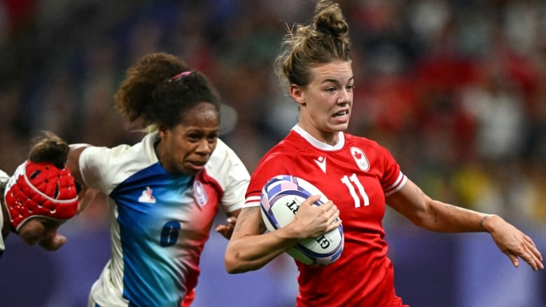 A woman's rugby player carries the ball while being chased down.