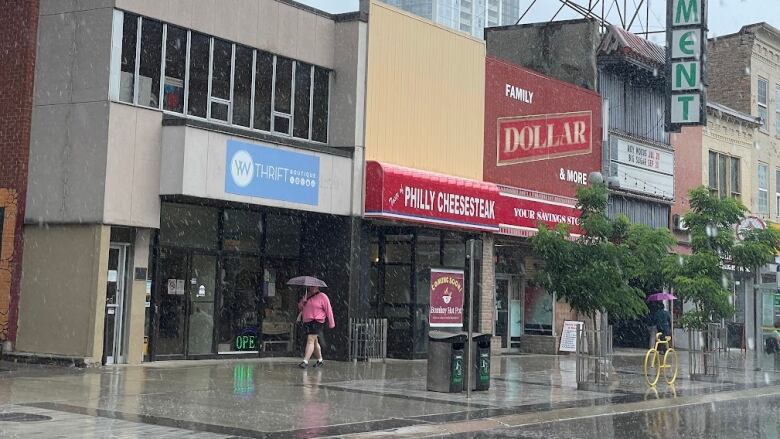 Downtown street, it's raining and a person walks down the street with an umbrella