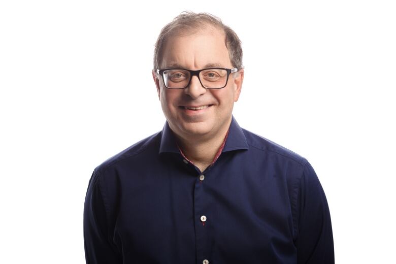 Man in a dark blue shirt and white background smiling at the camera.