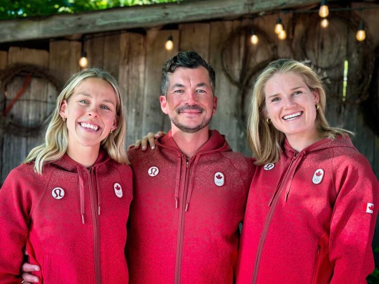 Man stands between two women smiling in Team Canada Olympic gear.