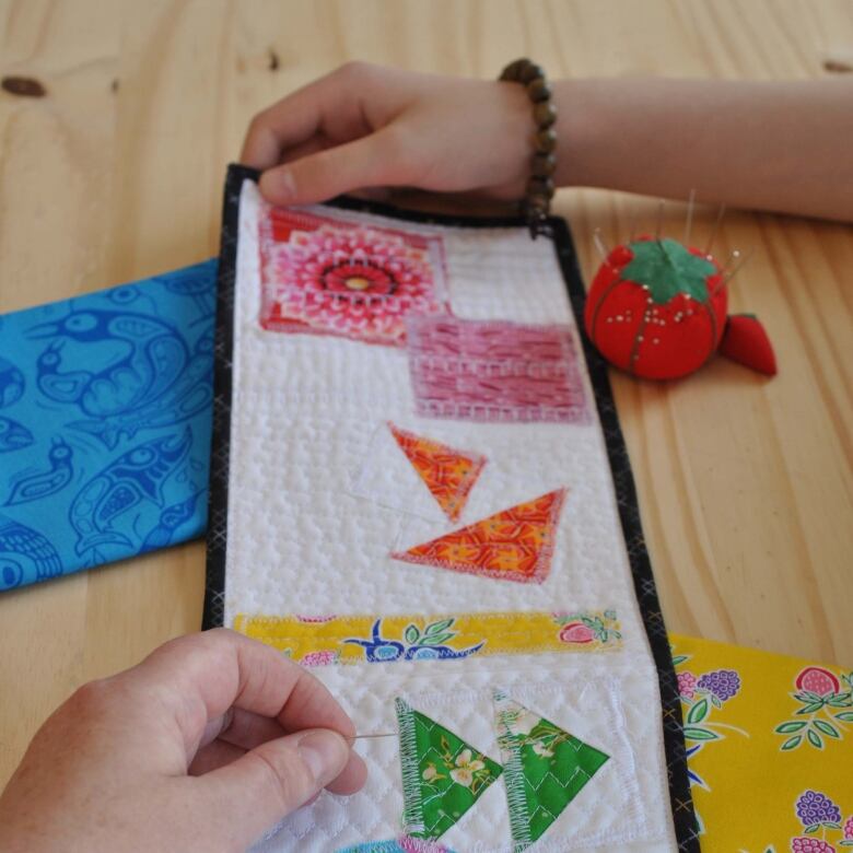 A photo of two hands holding up a sample quilt piece on a wooden table.