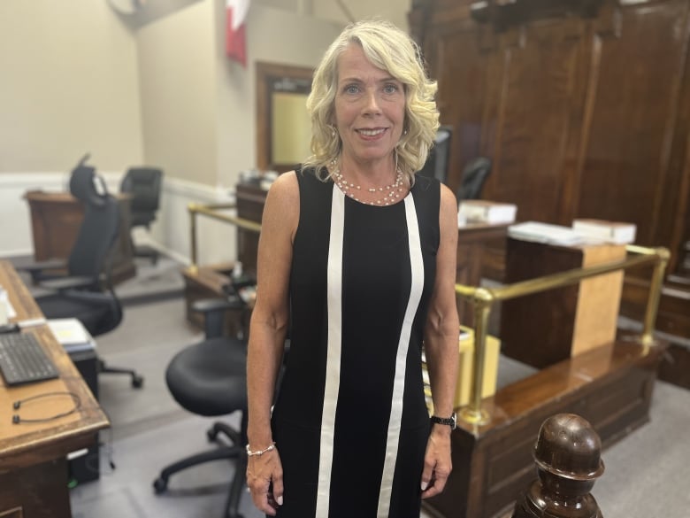 A woman in a black dress with two white stripes stands in the centre of a courtroom. 