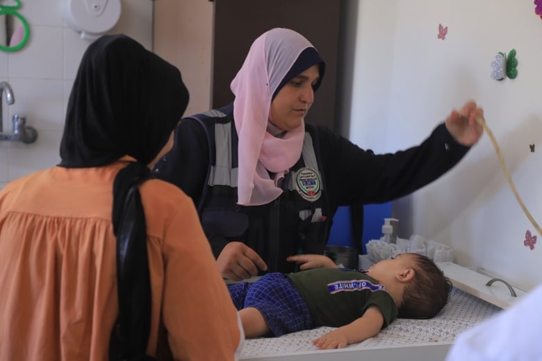 A woman in a pink headscarf and navy blue dress prepares a little boy on a stretcher for examination in a clinic