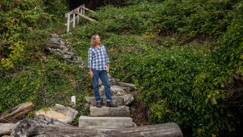 A man halfway down stone steps on a path surrounded by greenery peers into the distance.