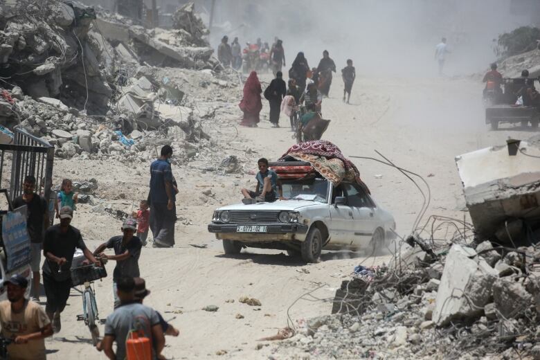 Several people are shown walking, with one vehicle in a dusty road with debris shown all around.