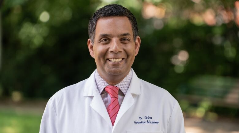 Man in white doctor's coat smiles into the camera.