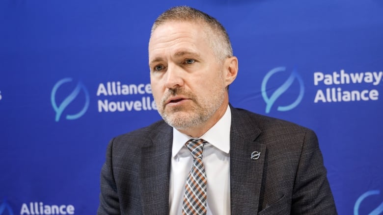 A man in a tie is pictured in front of a blue background.