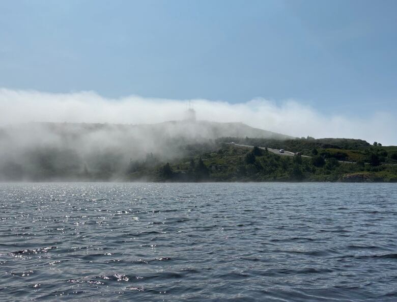 A pond in front of a hill blanketed by fog.