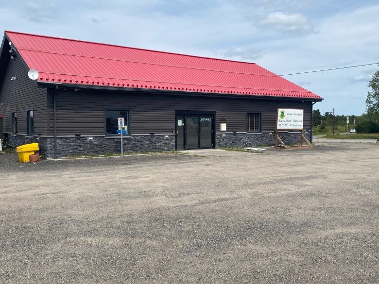 A newly built building with black siding and a red roof sits on a gravel parking lot.