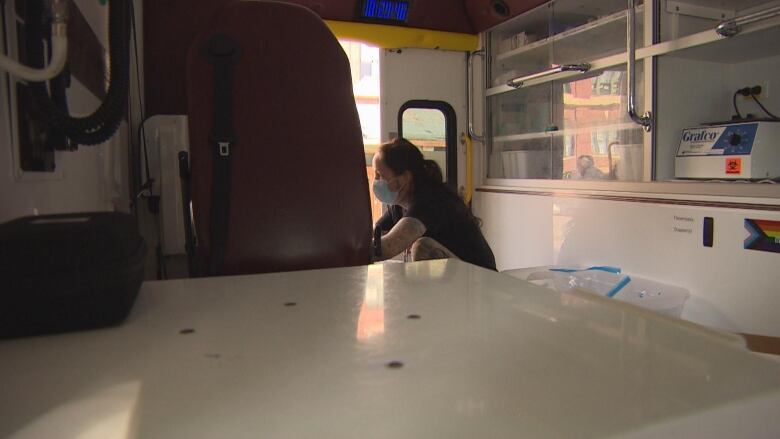 A woman with a mask inside the back of a van with shelves stocked with medical equipment.