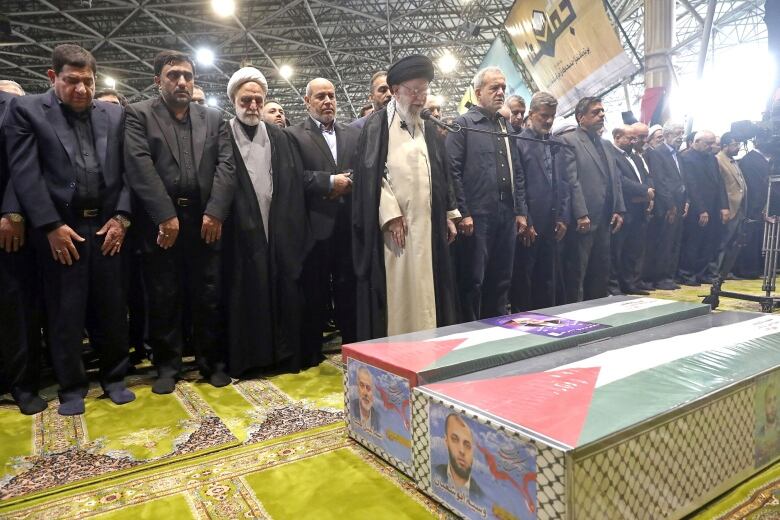 Several men in headresses and robes stand before a casket.